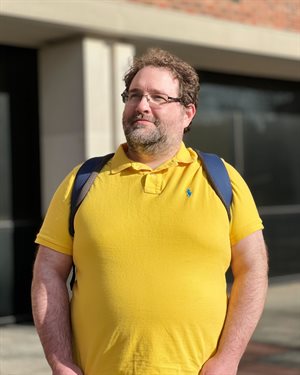 A photo of John Crockett in a yellow shirt with a blue backpack